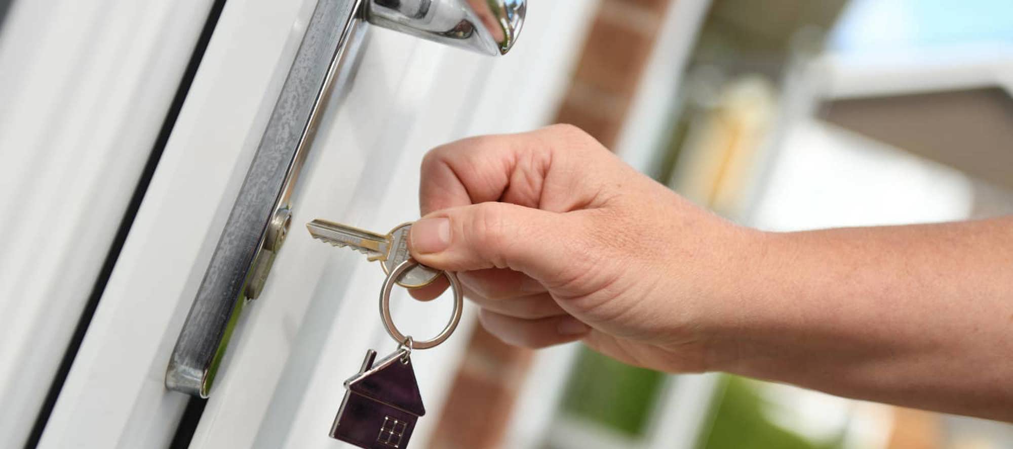 Close up of a key with a small house keyring being put into a front door